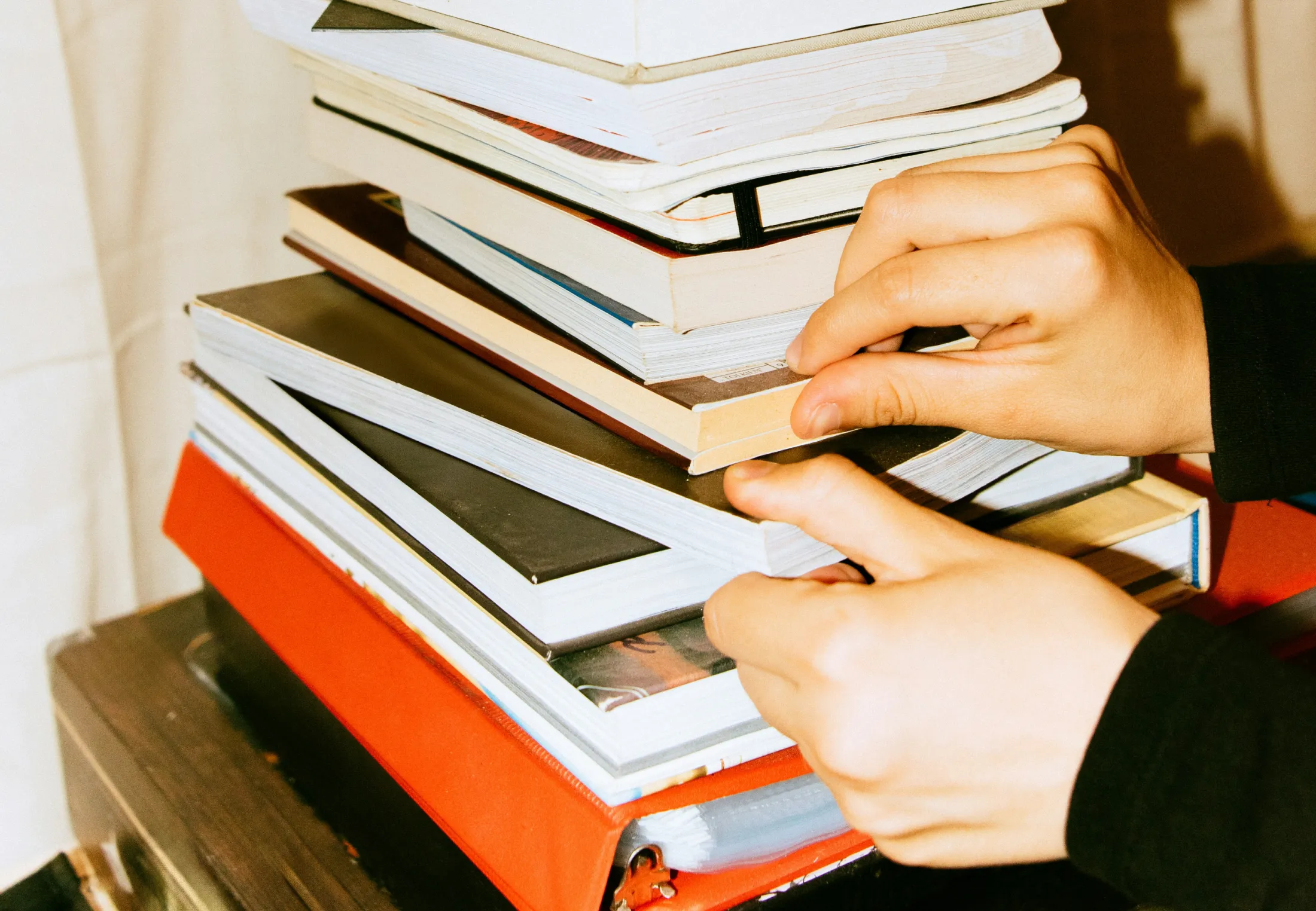 2 Hände greifen ein Buch aus der Mitte eines hohen Bücherstapels